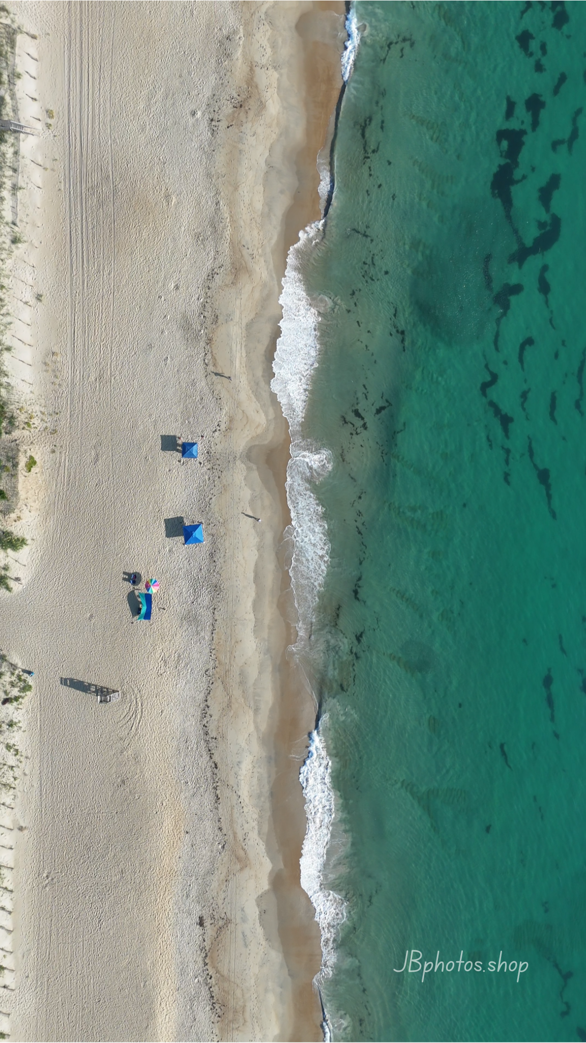 Aerial view of a beach with people and umbrellas near turquoise water.